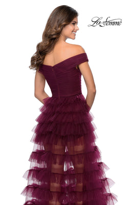 A woman wearing a La Femme 28804 long prom dress in burgundy, featuring an off-the-shoulder neckline and a layered, tiered tulle high-low skirt.