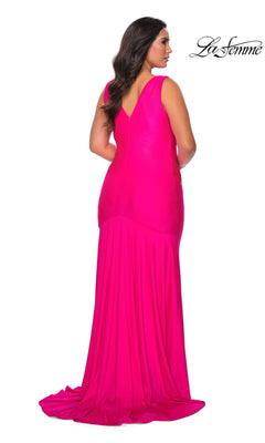 A woman wears the Long Plus-Size Prom Dress: La Femme 29016, a sleeveless, floor-length bright pink jersey gown with a V-neckline, faux wrap-style bodice, and pleated skirt.