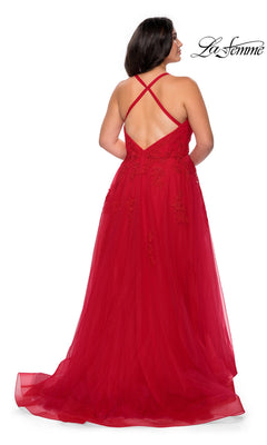 A woman is standing and facing away from the camera, wearing the La Femme Long Prom Dress 29021—a sleeveless red lace formal evening gown with a tulle skirt and a crisscross back design.