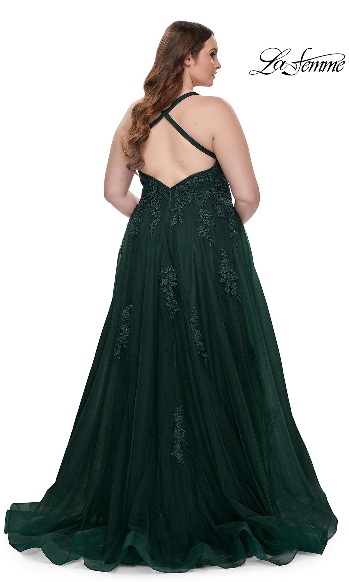 A woman with long brown hair models the La Femme Long Prom Dress 29021, a dark green, floor-length formal gown with lace accents and a crisscross open back, against a white background. 