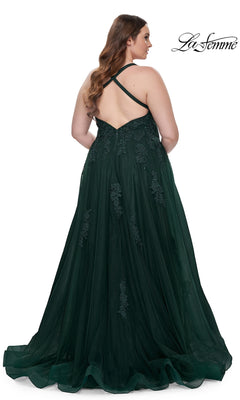 A woman with long brown hair models the La Femme Long Prom Dress 29021, a dark green, floor-length formal gown with lace accents and a crisscross open back, against a white background. "La Femme" appears in the top right corner.