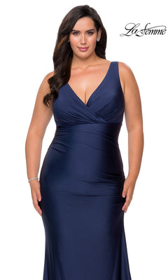 A woman wears a sleeveless navy blue floor-length Long Plus-Size Prom Dress: La Femme 29028 with a V-neckline and gathered waist detail in a jersey mermaid silhouette.