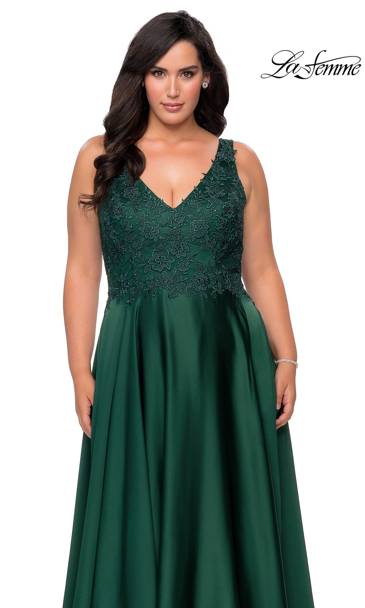A woman wearing a sleeveless, floor-length dark green Long Plus-Size Prom Dress: La Femme 29039 with a V-neckline and a rhinestone lace bodice.