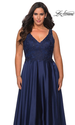 A woman wears a Long Plus-Size Prom Dress: La Femme 29039, a sleeveless, navy blue floor-length satin gown with a V-neckline and a bodice detailed with floral embroidery and sequins.