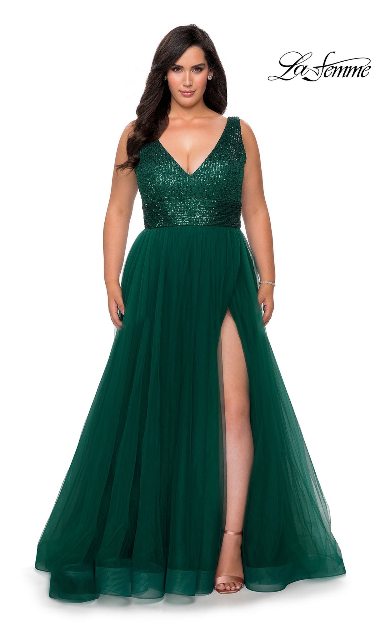 A woman in a sleeveless emerald green La Femme 29045 plus-size prom dress with sequin bodice and tulle A-line skirt stands in nude heels against a white background.