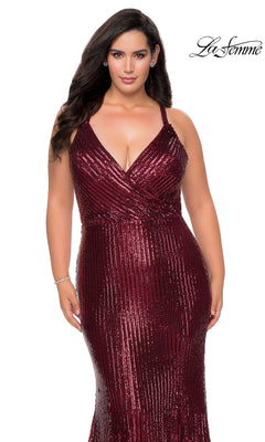 A person wearing the deep red, floor-length, sequin mermaid Long Plus-Size Prom Dress: La Femme 29051, featuring a V-neckline and a crisscross bodice.