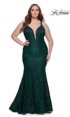 A woman in the La Femme Long Prom Dress 29052, featuring dark emerald floral lace, a plunging neckline, and thin straps, stands against a white background. The La Femme logo is shown in the top right corner.
