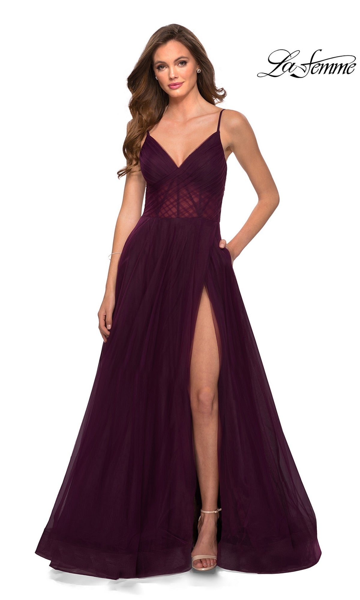 A woman in a La Femme Sheer-Waist Long A-Line Prom Dress 29076 in Dark Berry, featuring a V-neckline, thin straps, and high slit, stands against a plain white background.