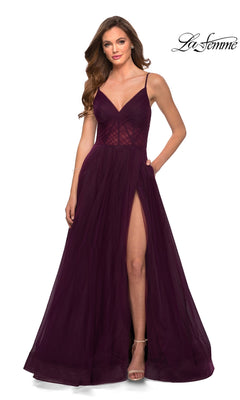 A woman in a La Femme Sheer-Waist Long A-Line Prom Dress 29076 in Dark Berry, featuring a V-neckline, thin straps, and high slit, stands against a plain white background.