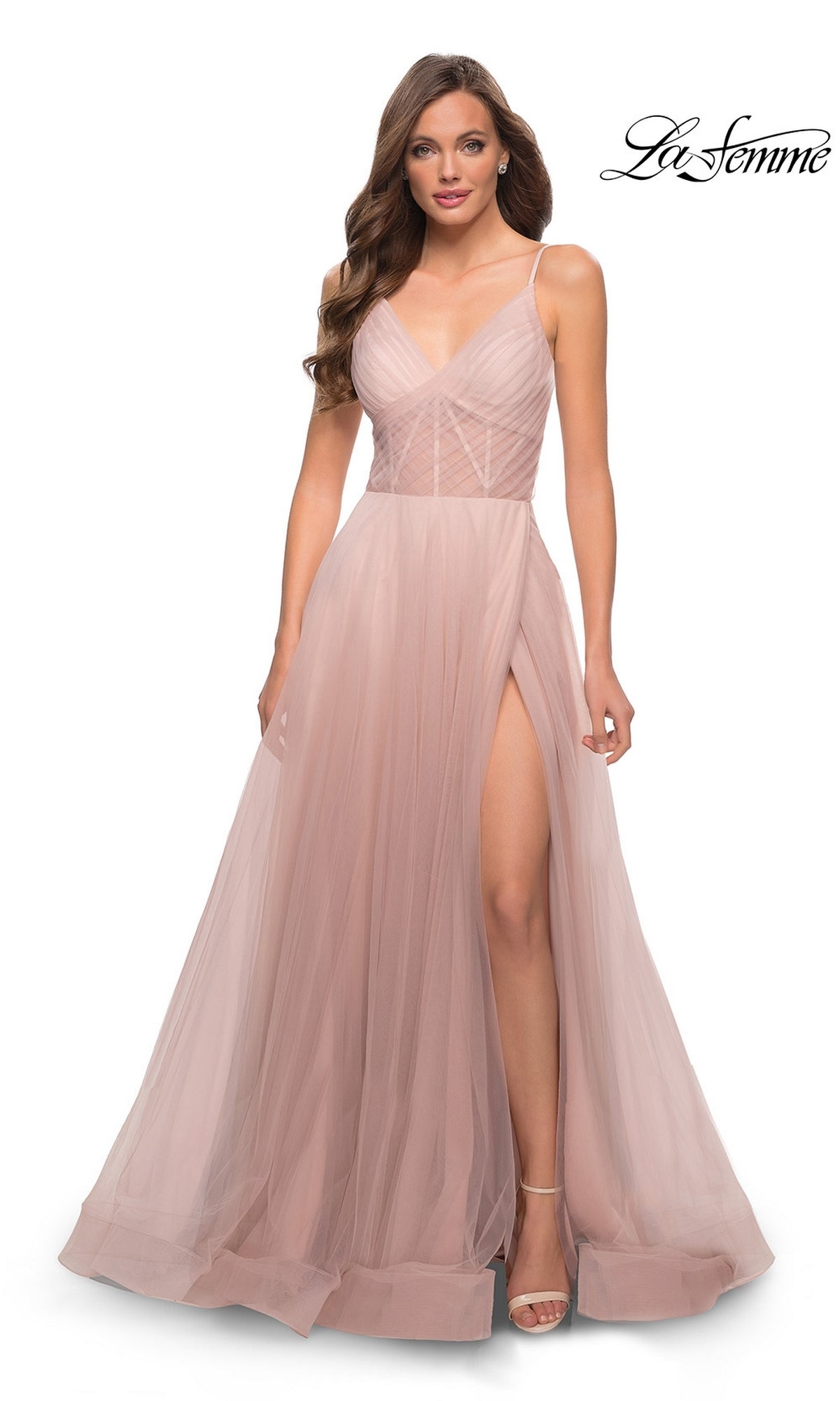 A woman wearing the La Femme Sheer-Waist Long A-Line Prom Dress 29076 in blush pink, featuring spaghetti straps, a fitted bodice, floor-length tulle skirt, and a high slit.