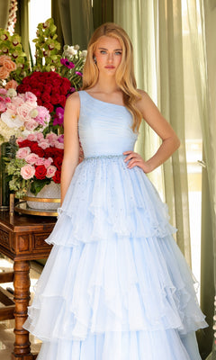 A young woman in the Ava Presley 29131 One-Shoulder Tiered Prom Gown stands indoors beside a table decorated with red, pink, and white floral arrangements.