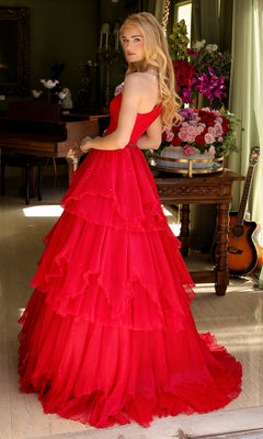 A woman wearing the Ava Presley 29131 One-Shoulder Tiered Prom Gown stands indoors by a table with flower arrangements and a guitar, gazing over her shoulder.