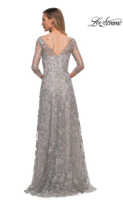 Woman in the Long Formal Dress: La Femme 29153—silver, floor-length with floral lace embroidery, sheer sleeves, and a deep V-back—stands with her back to the camera.