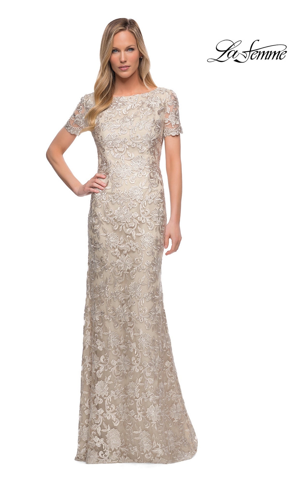 Woman wearing an elegant La Femme 29161 long formal dress—a floor-length, short-sleeve beige lace sheath evening gown adorned with delicate floral patterns; “La Femme” logo in the top right corner.
