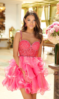 A young woman stands indoors in the Ava Presley 29179 Tiered Short Corset Hoco Dress, featuring bright pink ruffles, a beaded bodice, and spaghetti straps, surrounded by floral arrangements.