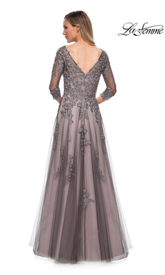 A woman wearing the La Femme 29205 long formal dress stands with her back to the camera, showcasing its delicate floral lace accents and V-shaped back. The elegant A-line tulle gown flows gracefully in soft grey, while the “La Femme” logo appears in the top right corner.