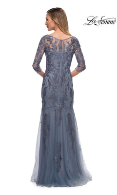Woman in Long Formal Dress: La Femme 29226, blue lace with sheer sleeves and floral embroidery, standing with back to camera. “La Femme” logo top right.