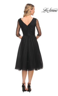 Woman in Knee Length Wedding Guest Dress: La Femme 29229 with sheer three-quarter sleeves and v-neck back, paired with black heels.