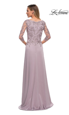 Woman faces away in a floor-length, light lavender lace dress with sheer embroidered sleeves. “La Femme” logo top right. Product: Long Formal Dress: La Femme 29251.