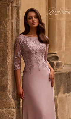 A woman in a mauve Long Formal Dress: La Femme 29251 with three-quarter lace sleeves stands gracefully by a stone column.