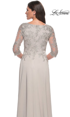 A woman in a light gray Long Formal Dress: La Femme 29251 with sheer, embroidered sleeves and back stands with her back to the camera—ideal for mothers of the bride.