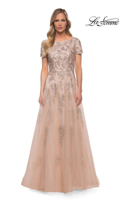 Woman in a floor-length, short-sleeve nude tulle Long Formal Dress: La Femme 29290 with silver floral embroidery, standing against a white background. “La Femme” logo in top right.