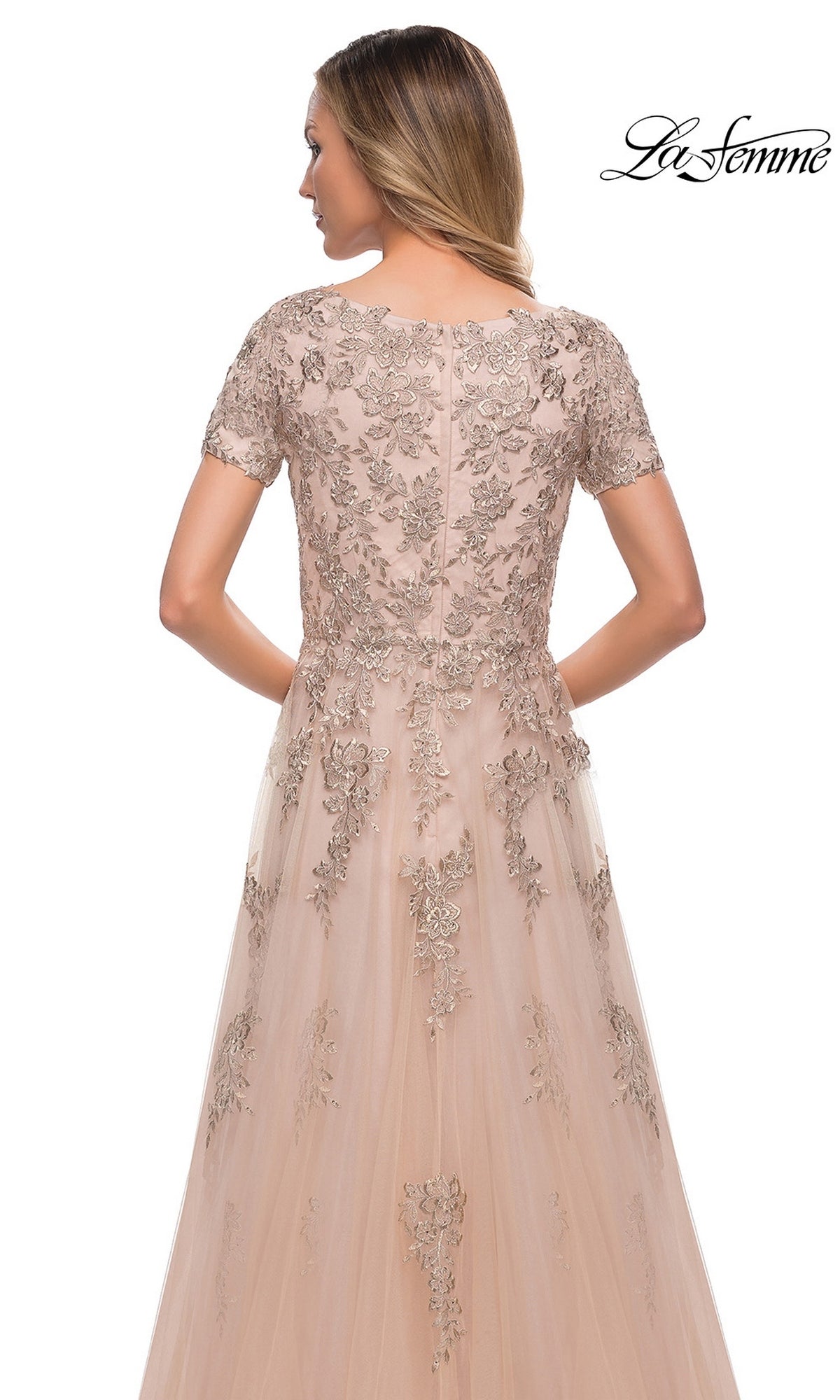 Woman wearing Long Formal Dress: La Femme 29290, a light pink tulle evening gown with silver floral embroidery, shown from the back on a white background.