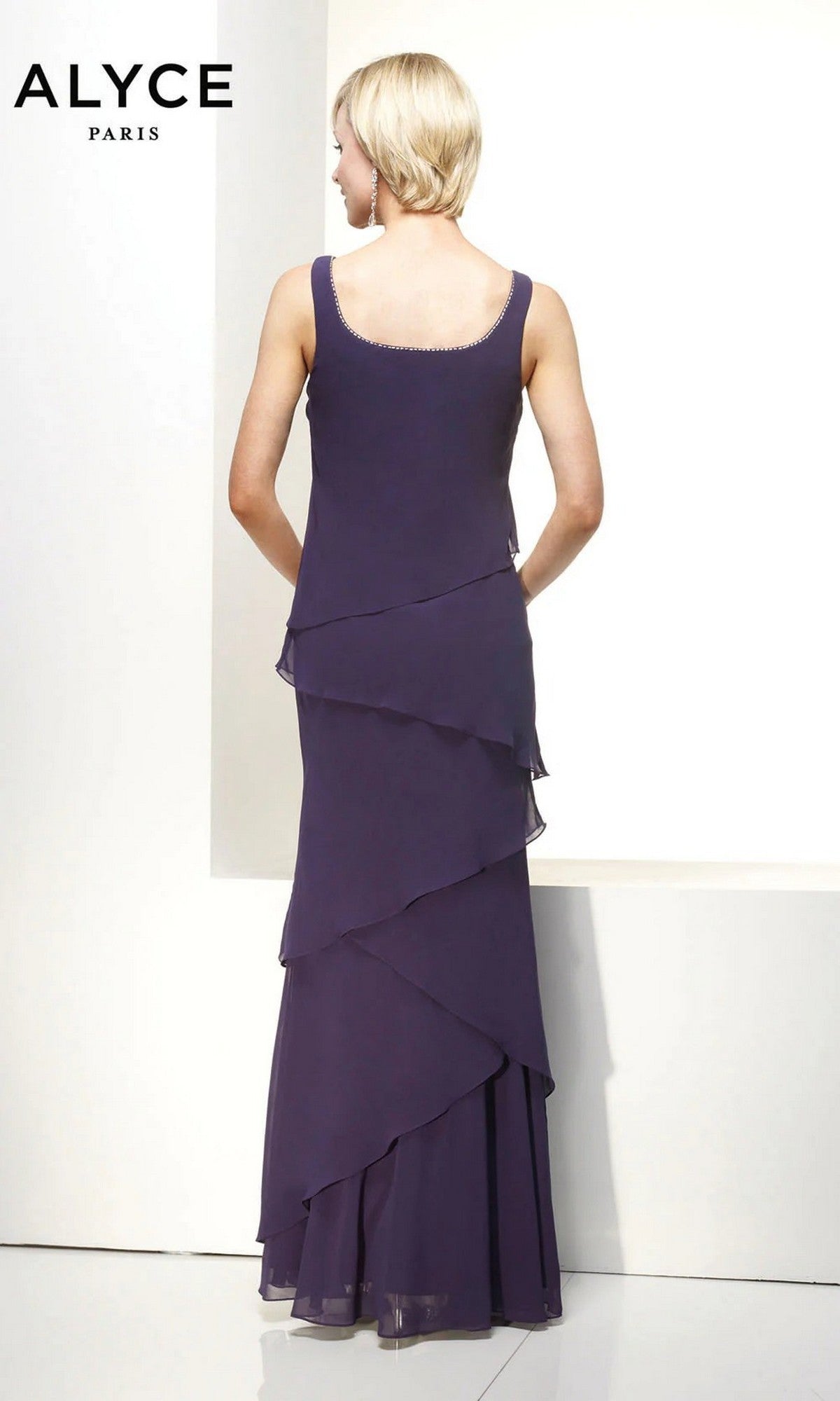 A woman in the Alyce 29292 long formal dress stands with her back to the camera, wearing a sleeveless, floor-length, layered purple chiffon gown. 