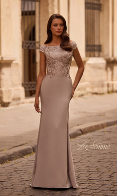 Woman wearing Long Formal Dress: La Femme 29331 in light taupe, with a fitted embroidered bodice and cap sleeves, stands on a cobblestone street by a light-colored building.