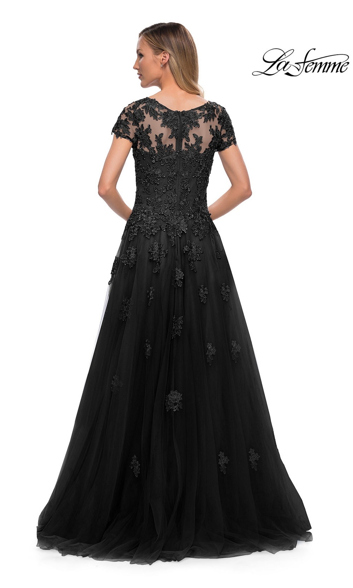 Woman wearing the Long Formal Dress: La Femme 29380, featuring tulle, floral lace appliques, and a sheer back panel, stands with her back to the camera.