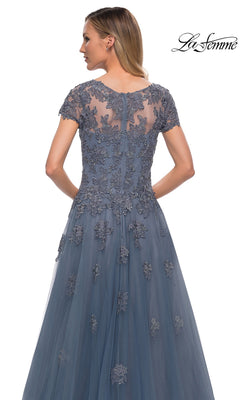 A woman in a blue Long Formal Dress: La Femme 29380 with lace appliques and floral embroidery stands facing away. The “La Femme” logo is in the top right corner.