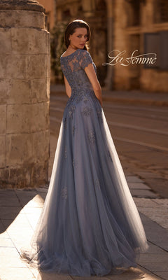 Woman in a Long Formal Dress: La Femme 29380 with lace appliques stands outdoors on a stone path, facing away.