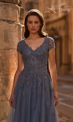 A woman in an A-line, lace-detailed blue Long Formal Dress: La Femme 29380 stands outdoors by a stone wall. “La Femme” appears in the top right corner.