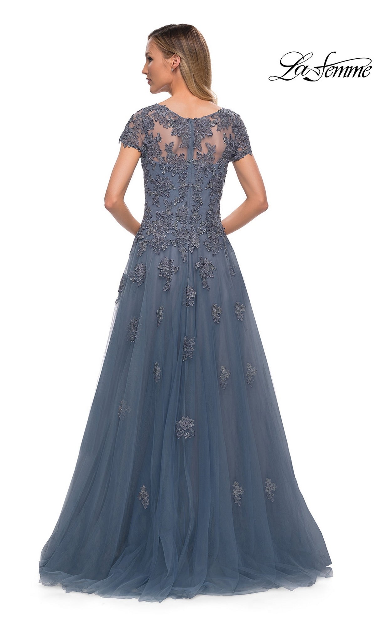 Woman in the Long Formal Dress: La Femme 29380, a floor-length blue gown with lace appliques and sheer back, stands with her back to the camera.