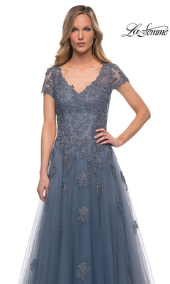 Woman wearing Long Formal Dress: La Femme 29380—slate blue, floor-length tulle with lace appliqué, short sleeves, V-neck—posing against a white background. “La Femme” logo top right.