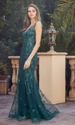 Outdoors, a woman wears the Glitter-Print Long Prom Dress: Juliet 294—a sleeveless, floor-length emerald green gown with floral embellishments. Lush greenery and a lantern decorate the background.