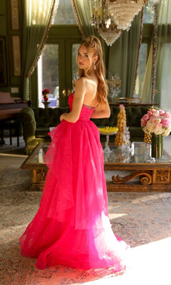 A woman in the Ava Presley 29524 strapless long prom ball gown poses indoors, glancing over her shoulder in a room with green walls, large windows, ornate curtains, and a chandelier.