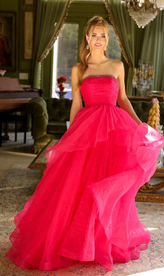 A woman stands indoors in the Ava Presley 29524—a strapless bright pink a-line ball gown with layered tulle and beaded accents—holding the skirt with one hand.