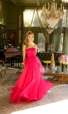 A woman wears the strapless long prom ball gown Ava Presley 29524 in a sunlit room with chandeliers, antique furniture, and large windows.