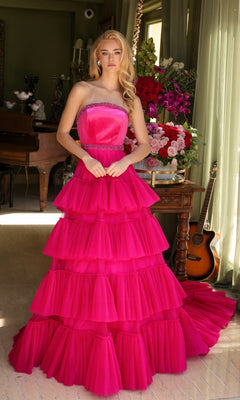 A woman wearing the Long Prom Dress 29529 by Ava Presley—a strapless, bright pink layered ruffle ball gown—stands indoors near a table with flowers, with a guitar and piano in the background.