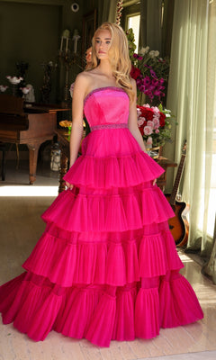 A person stands indoors wearing the Long Prom Dress 29529 by Ava Presley, a strapless bright pink A-line dress with pleated layers, surrounded by flowers and musical instruments.