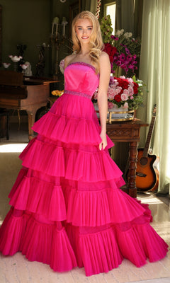 A woman stands indoors in the Long Prom Dress 29529 by Ava Presley, a bright pink, layered ruffle ball gown, with flowers, a guitar, and a piano in the background.