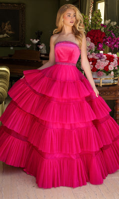 A woman stands indoors wearing the Long Prom Dress 29529 by Ava Presley, a strapless bright pink A-line dress with a multi-tiered ruffled skirt. In the background are a table with flower arrangements and a painting.