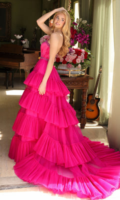 A woman poses indoors by a window with flowers, a table, and a guitar in the background, wearing the Long Prom Dress 29529 by Ava Presley—a bright pink layered ruffle ball gown.