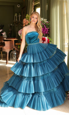 A woman wears the Long Prom Dress 29529 by Ava Presley, a strapless A-line gown with a layered ruffle ball skirt, standing indoors near a window and flowers with a grand piano and floral decor in the background.