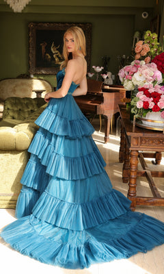 A woman in the Long Prom Dress 29529 by Ava Presley stands indoors near a green sofa and a flower-filled table, with a piano and painting visible in the background.