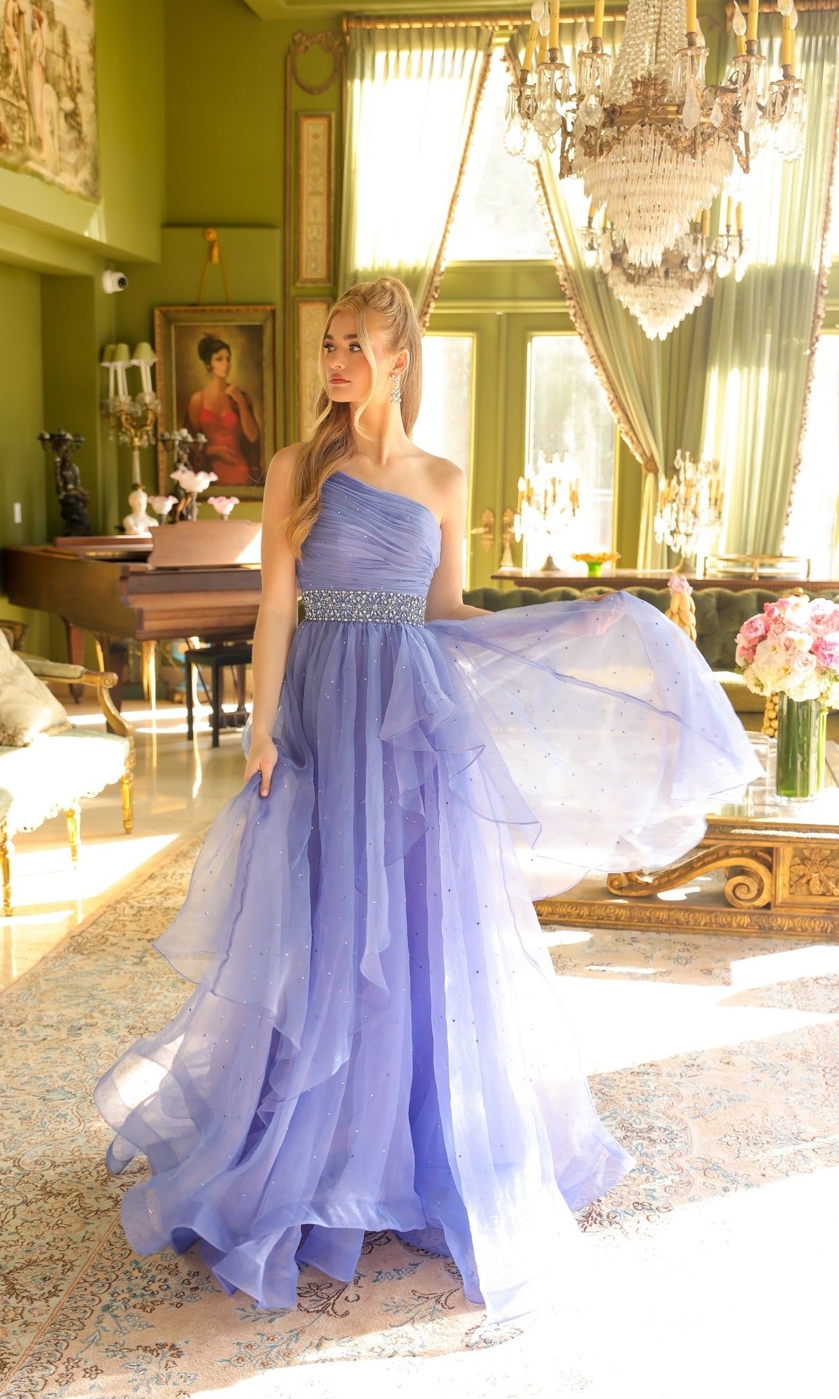 A woman in the Ava Presley 29534 beaded-waist long prom dress stands in a sunlit, elegant room with large windows, a chandelier, and classical decor.