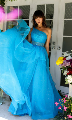 A woman in the Ava Presley 29534 Beaded-Waist Long Prom Dress stands by white doors, holding up her blue one-shoulder gown next to a vase of colorful flowers.