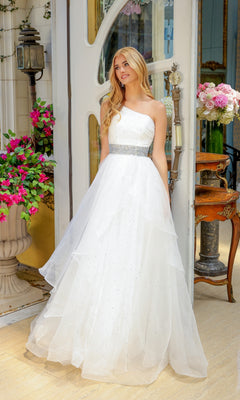 A woman in the Ava Presley 29534 Beaded-Waist Long Prom Dress stands indoors near a door, surrounded by potted flowers and vintage decor.