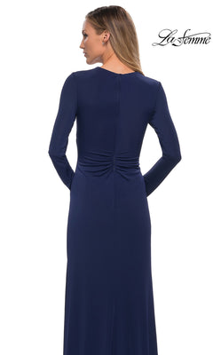 A woman seen from the back wearing a navy blue, long-sleeve, floor-length La Femme 29535 gown with ruched detailing at the lower back.